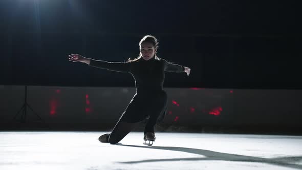 Beautiful Young Sportswoman is Skating on Ice Rink in Darkness Performing Elements of Figure Skating alt