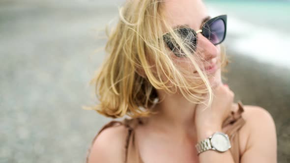 Attractive Girl in Sunglasses with Blond Hair Closeup By the Sea Wind Develops Her Hair