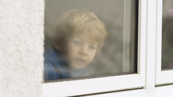 Little blond boy looking out the window while snowfall outside