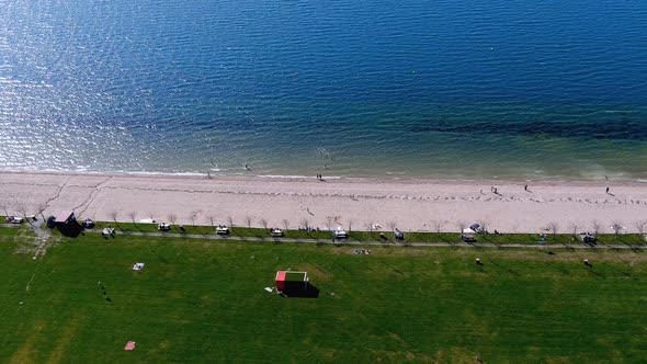 Lake beach with people sunbathing and bathing, garden and walking area. Overhead drone shot travelin alt