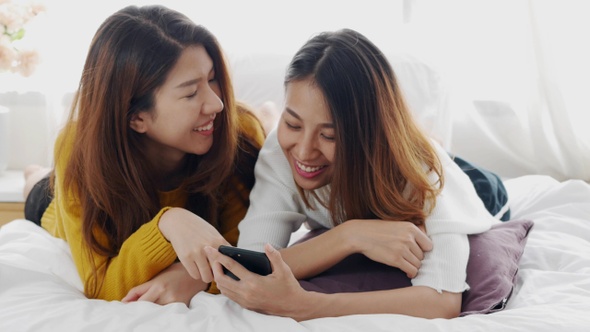 Young Asian lesbian couple using an app on smartphone in a bedroom at home.