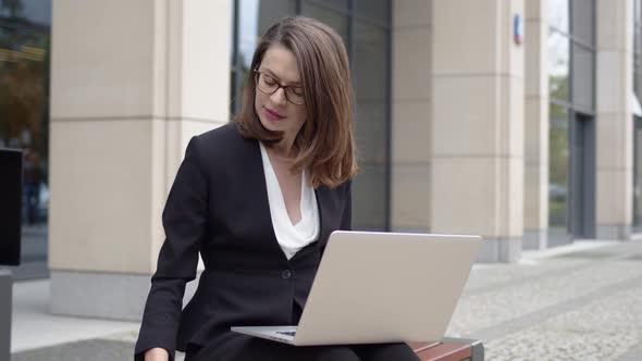 Woman in Formal Attire Using Laptop Outside Office Building