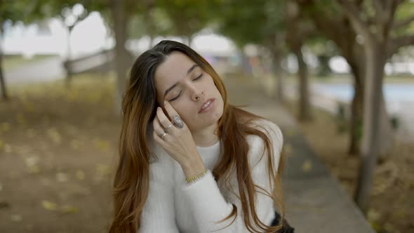 Close View of Young Brownhaired Woman in Park Touching Her Face alt
