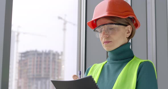 Portrait of a working woman builder in a helmet writing notes in a notebook. alt