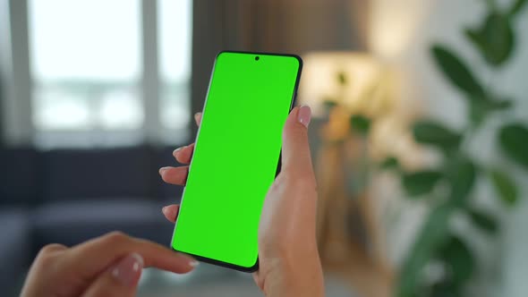 Woman at Home Using Smartphone with Green Mockup Screen in Vertical Mode alt