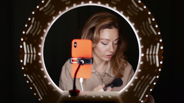 View of Cute Female Blogger Contouring Face in Front of Ring Light with Phone