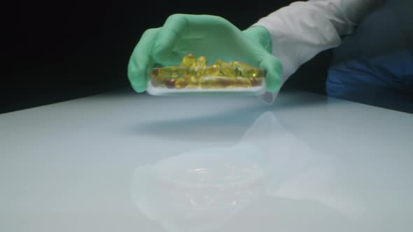 Lab Technician Putting Dish with Oil Capsules on White Table alt