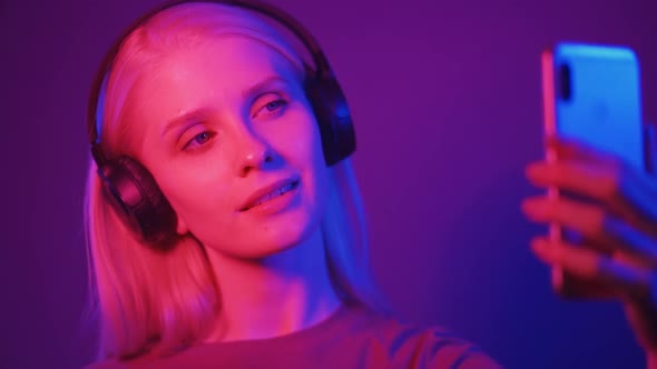 Beautiful Joyful Woman Dancing with Headphones and Filming Herself Using the Phone in Neon Light