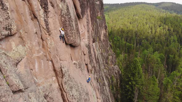 Two Men Are Climbing a Vertical Granite Wall in the Middle of a Forest.