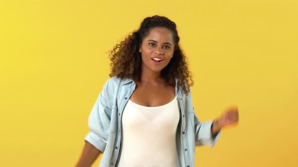 Happy smiling African American woman dancing with funny movement isolated on yellow background