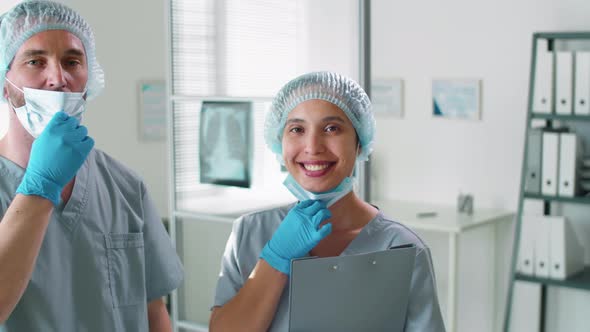 Positive Male and Female Doctors Taking Masks Off and Smiling at Camera alt