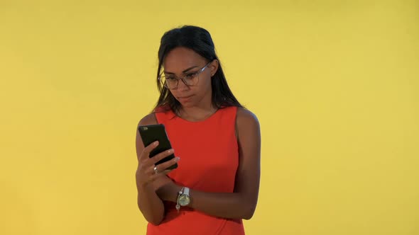 Multiracial Pretty Woman Looking Surprised at Smartphone on Yellow Background alt