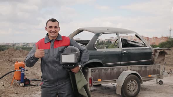 Portrait of industrial worker in overall looks to the camera and smile and shows thumb up alt