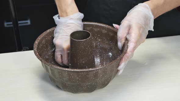 Gloved Hands of a Pastry Chef Butter the Surface of a Donutshaped Cake Pan alt