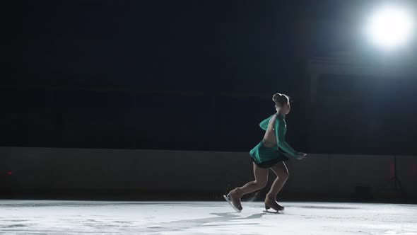 The Girl Skater Performs a Jump with the Rotation of a Triple Toe Loop in a Counter Light on an Ice alt
