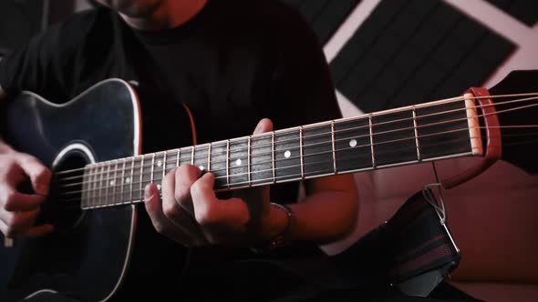 Young Man Playing Acoustic Guitar While Sitting on Sofa in Home Recording Studio alt