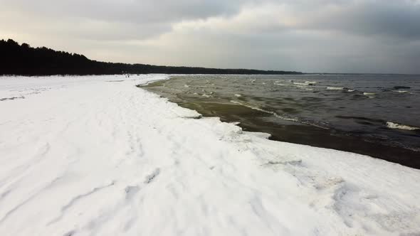 The waves of the sea roll onto the shore of the snow cover