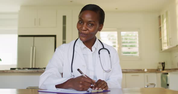 Smiling african american female doctor making notes during video call consultation alt