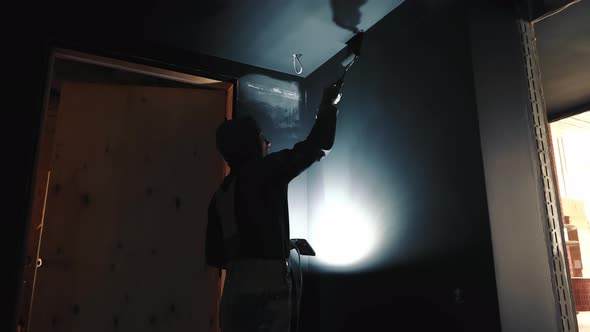 Painter on Construction Site Paints Walls in the Dark Illuminates with a Lamp alt