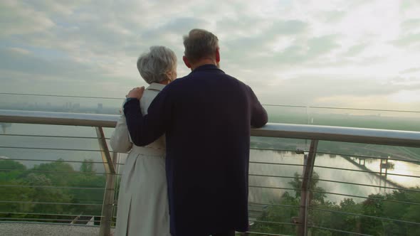 Mature Couple Standing on Terrace Hugging and Looking on City Beauty alt