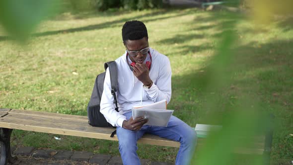 Busy Concentrated African American Student Learning Outdoors Sitting on Bench at College Yard alt