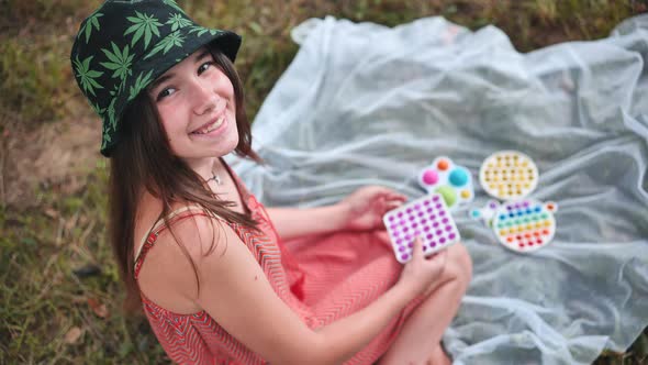 Smiling Girl Plays with Antistress Toys Popit and Simple Dimple in the Park on a Summer Day alt