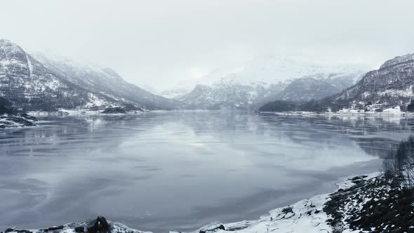 Flying above a frosen lake between Mountains in fogy day in Norway in december 2018 alt