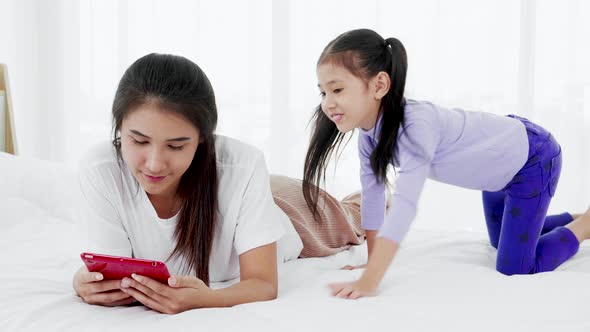 mother and young child lying on bed while playing on tablet in the daytime