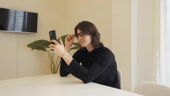 Young man with glasses on a video call using his mobile phone, sitting at a table alt