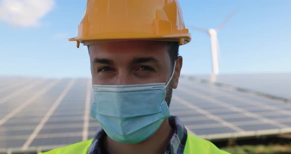 Young man working at solar power station while wearing safety face mask alt
