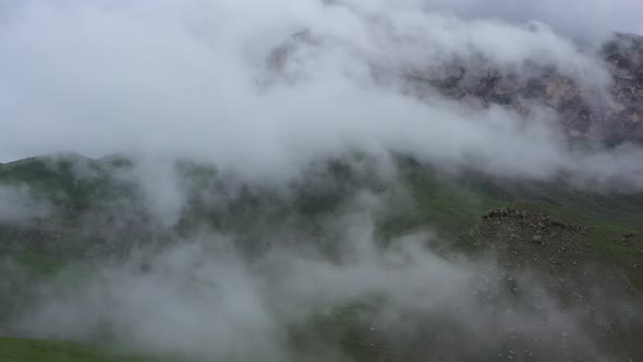 Drone Flight above green fields at the mountains in the clouds and fog.