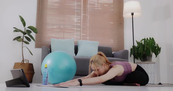 Young Asian woman in sportswear doing exercise and watching fitness tutorial online video on tablet. alt