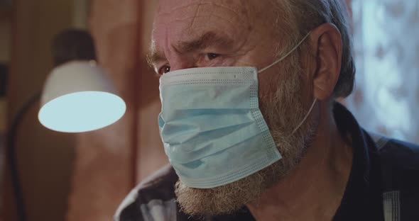 Portrait of Sad Older Man in Medical Mask Thoughtfully Looks at Camera alt
