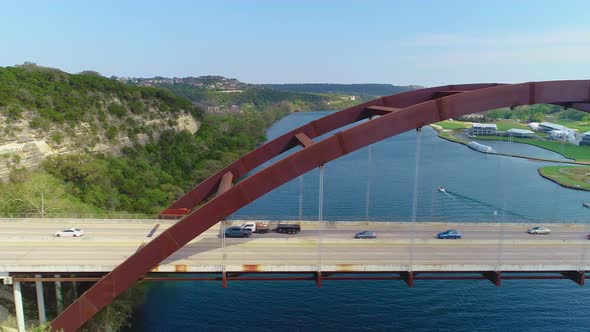 Minor traffic moving from left to right on the Pennybacker Bridge with a view of the city of Austin, alt