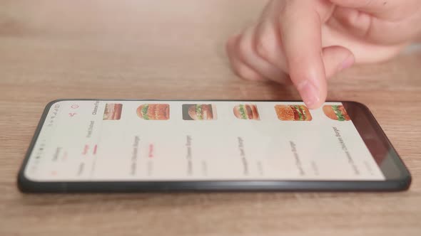 Close Up Of Hand Male Selects Food In Food Online Delivery Apps Directly On Smartphone alt