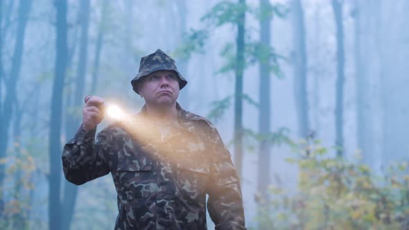 A Man with a Flashlight in His Hand Walks Through the Forest in the Fog. Searches in the Forest alt