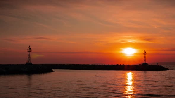 High Lighthouse Silhouette on Rocky Cliff at Calm Sea Against Sunset alt