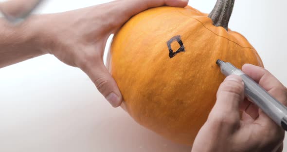 A Young Man's Hands Holding a Black Marker Drawing Eyes and Mouth on a Large Pumpkin