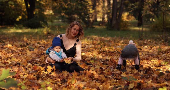 Gorgeous Young Mother with Two Kids Enjoying Sunny Autumn Day on the Foliage