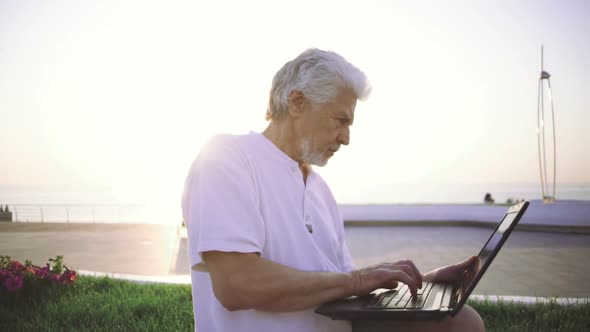 Portrait of Retirement Handsome Senior Man Using Laptop Computer on Seafront alt