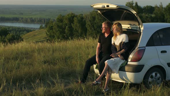 beautiful couple chatting sitting in the trunk of a car at the break