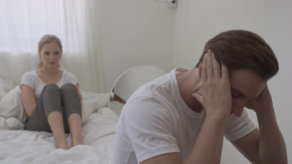 Upset boyfriend sitting on the bed after argument with his girlfriend
