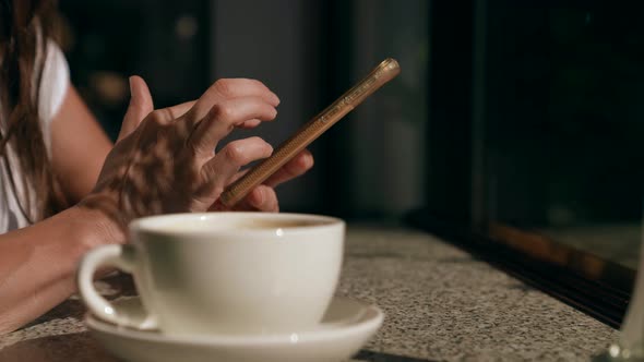 Woman is Resting in Cafe Have a Break at Daytime Closeup of Hands with Smartphone and White Cup alt