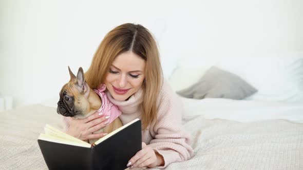 A Woman in a Cozy Powder Pink Sweater and White Stockings Lying on the Bed with Her Dog and Reads alt