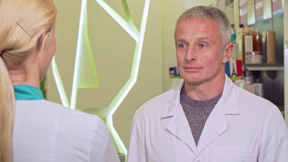 Cheerful Senior Male Chemist Talking To His Colleague at Drugstore alt