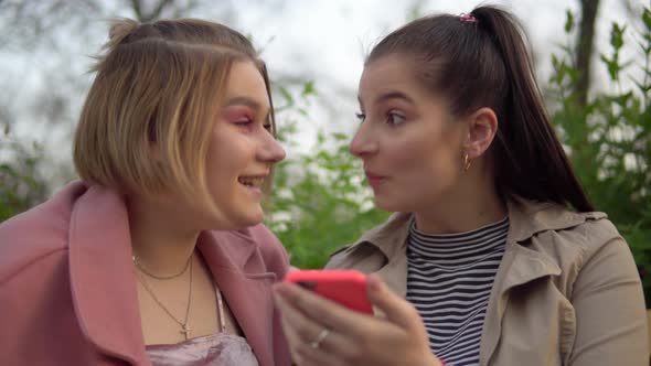 Young Women Friends Looking at Mobile Phone Walking in Park