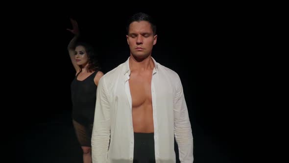 Wary Young Man on Dark Stage in White Shirt Naked Torsoturning Head From Side to Sidebehind Him