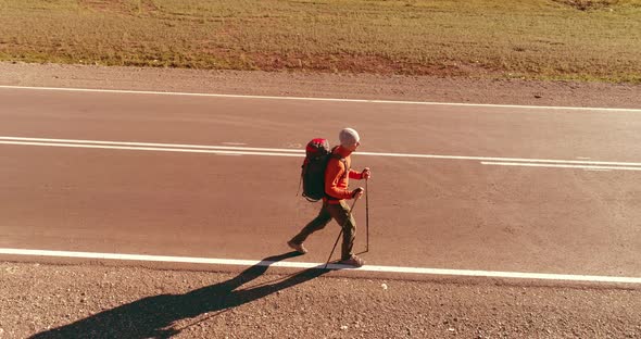 Flight Over Hitchhiker Tourist Walking on Asphalt Road. Huge Rural Valley at Summer Day. Backpack alt