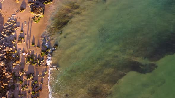 Amazing scenic drone aerial view of the beach and ocean with calm waves during a sunset.