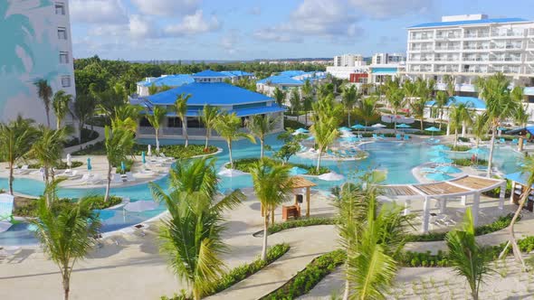 Aerial panning shot showing empty swimming pools with palm trees during sunny day - Covid-19 Pandemi alt